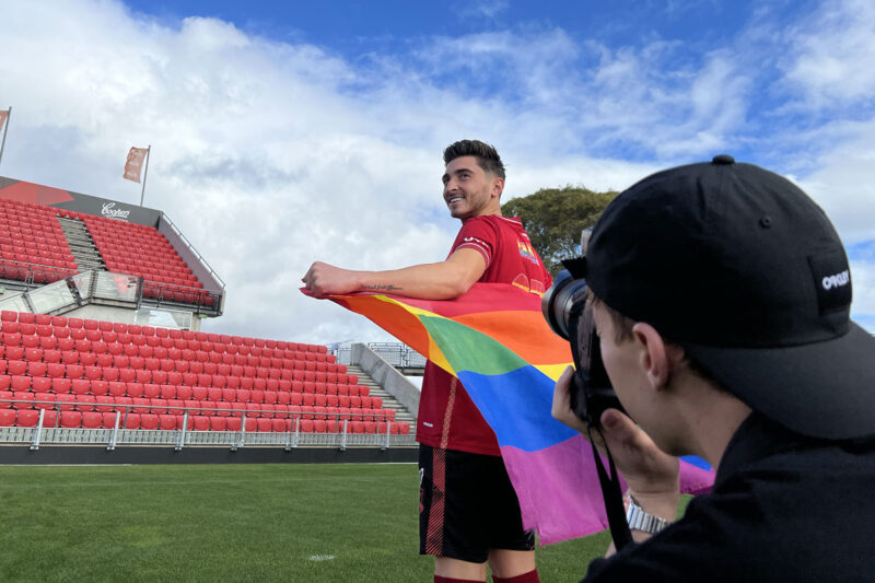 Josh Cavallo on an oval waving a rainbow flag